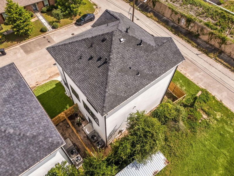 A beautiful aerial view from behind the home highlights the property's exterior, corner lot setting, and surrounding views beneath blue skies.