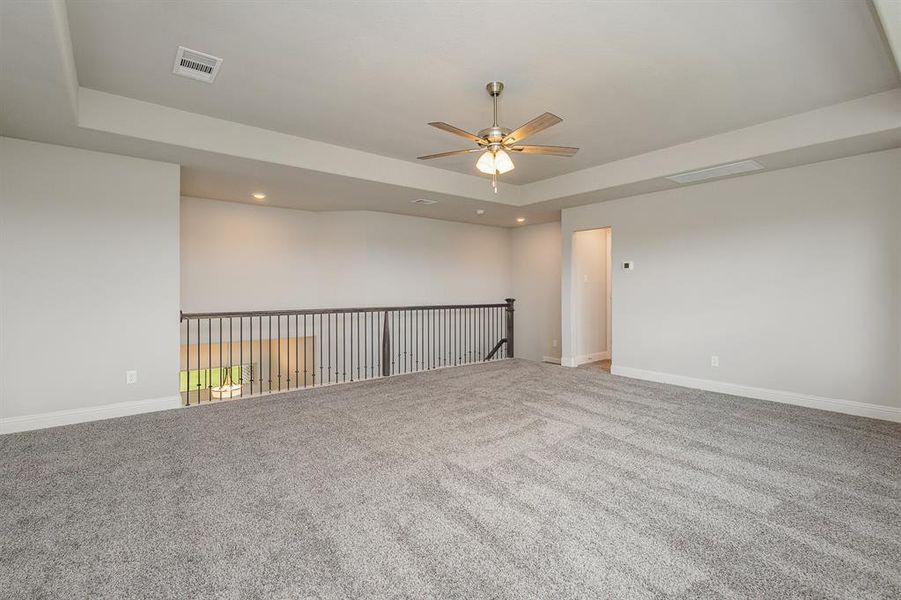 Carpeted empty room with ceiling fan and a raised ceiling