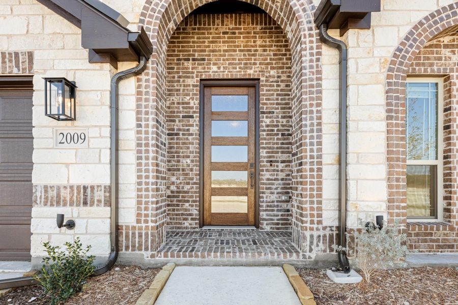 Home entrance with brick arched entryway, wood and glass front door, and stone exterior accents