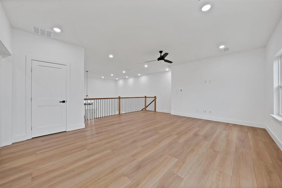 Spacious open-concept room featuring light wood-finish flooring, recessed lighting, and a modern ceiling fan