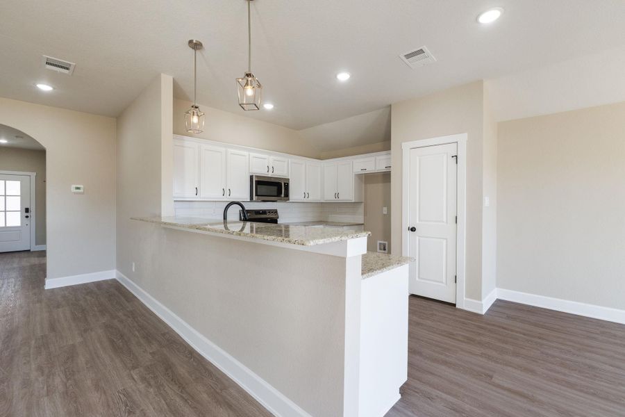 Kitchen featuring arched walkways, light stone countertops, white cabinets, a peninsula, and pendant lighting
