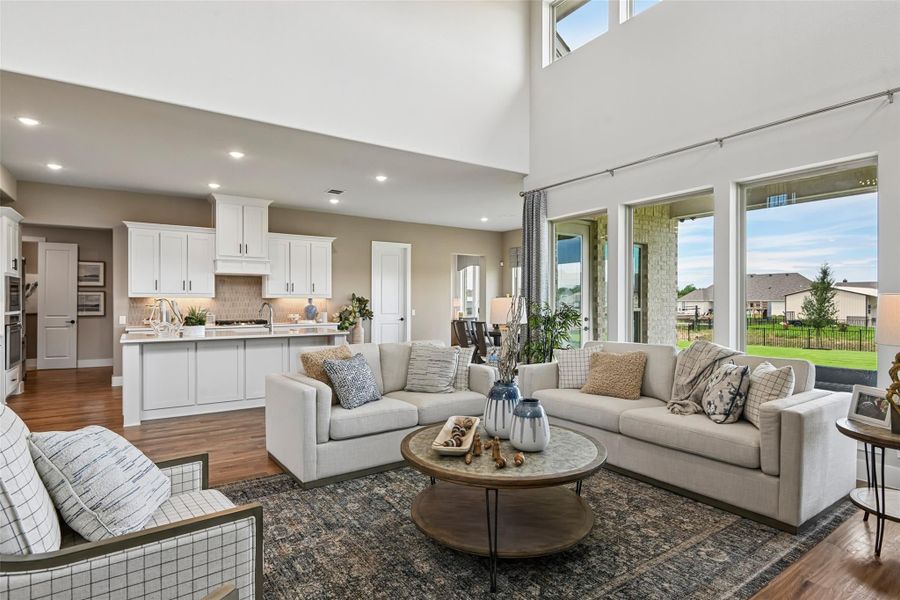 Open-concept living room with high ceilings, hardwood floors, and kitchen visible in background Open-concept living room with high ceilings, hardwood floors, and kitchen visible in background