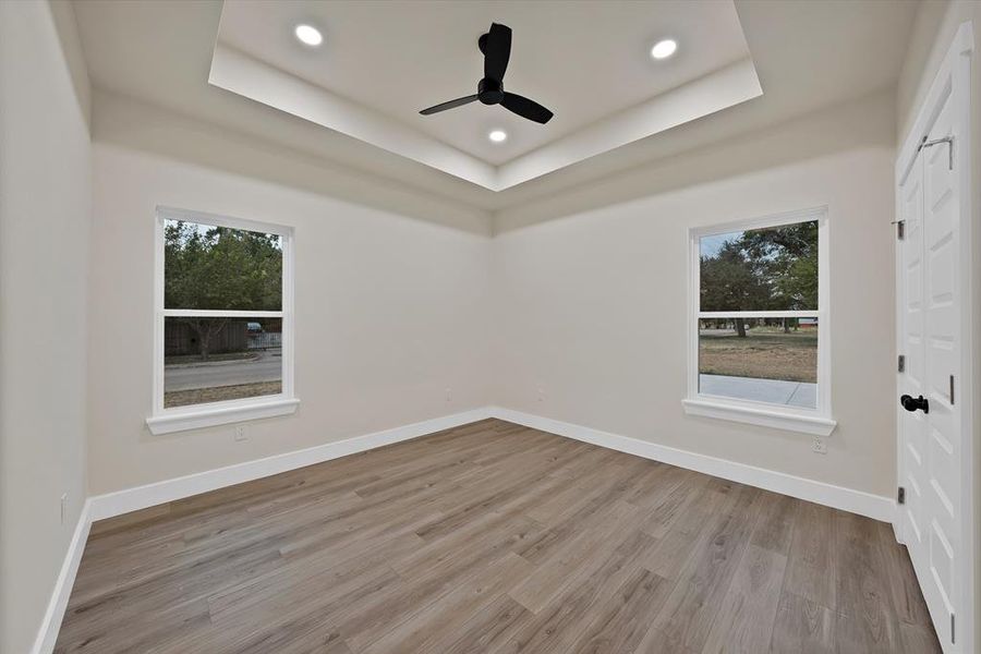 Unfurnished room featuring a raised ceiling, healthy amount of natural light, light wood-style floors, and recessed lighting