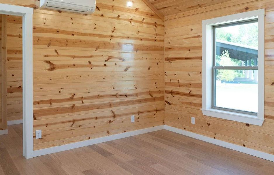 Empty room with wood finished floors, wooden walls, an AC wall unit, and vaulted ceiling Empty room with wood finished floors, wooden walls, an AC wall unit, and vaulted ceiling