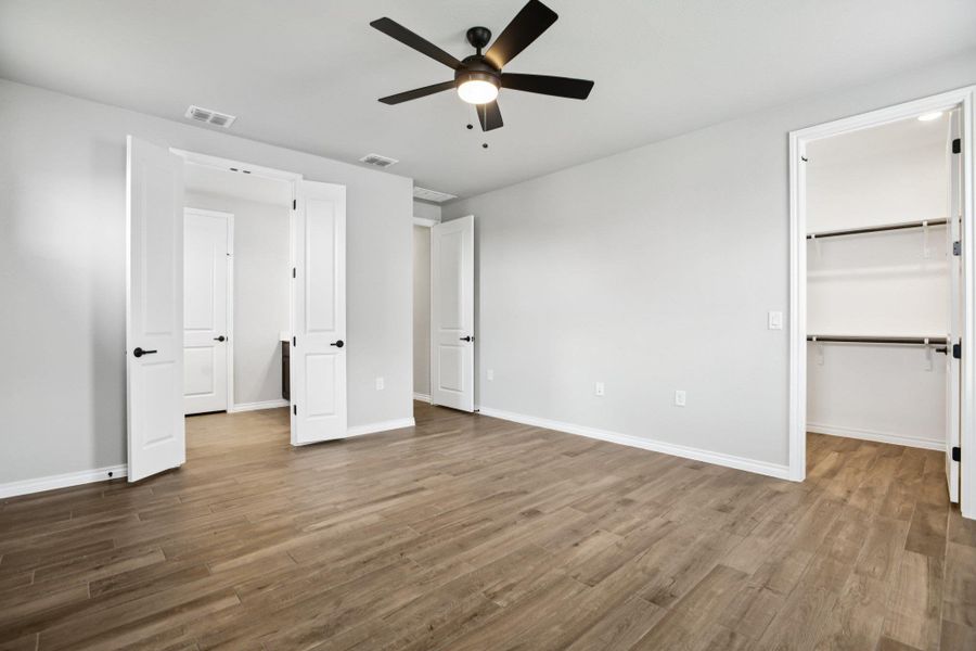 Unfurnished bedroom featuring a spacious closet, wood finished floors, and a ceiling fan Unfurnished bedroom featuring a spacious closet, wood finished floors, and a ceiling fan