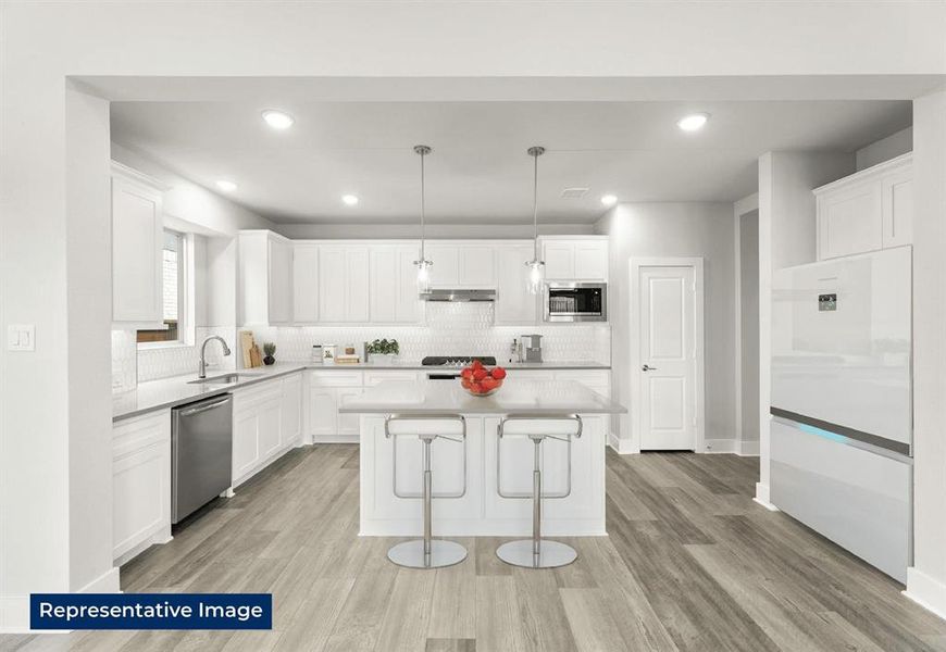 Kitchen with white cabinets, a kitchen bar, light wood-style flooring, a center island, and stainless steel appliances
