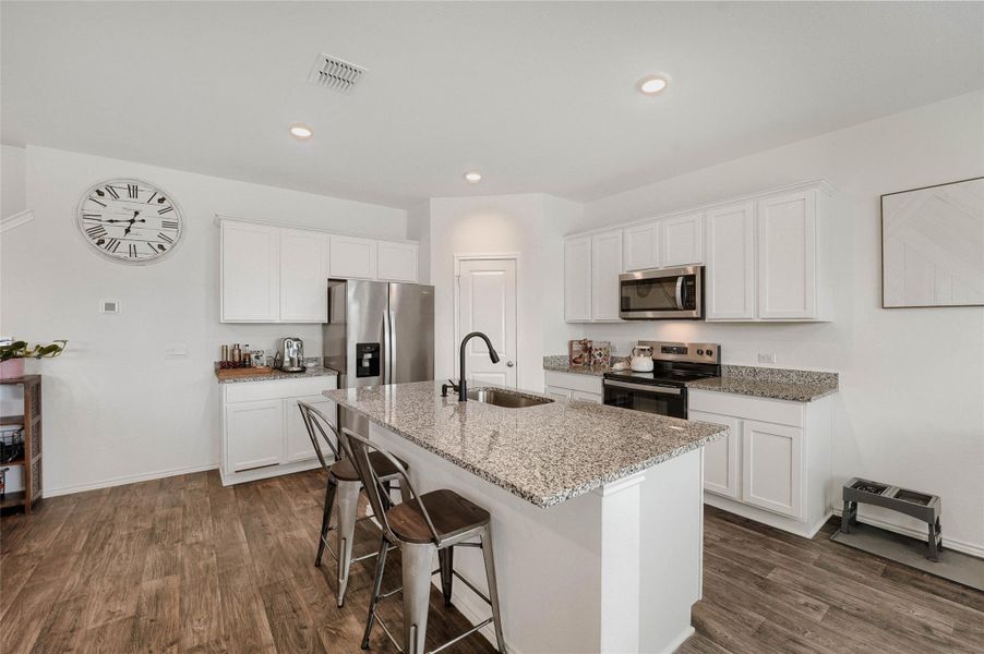 Kitchen featuring wood-finish flooring, white cabinetry, a central island with a granite countertop and undermount sink, and stainless steel appliances Kitchen featuring wood-finish flooring, white cabinetry, a central island with a granite countertop and undermount sink, and stainless steel appliances