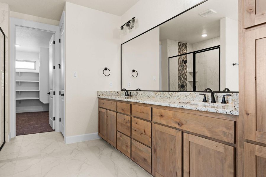 Full bath with light marble finish flooring, double vanity, a marble finish shower, and a spacious closet Full bath with light marble finish flooring, double vanity, a marble finish shower, and a spacious closet