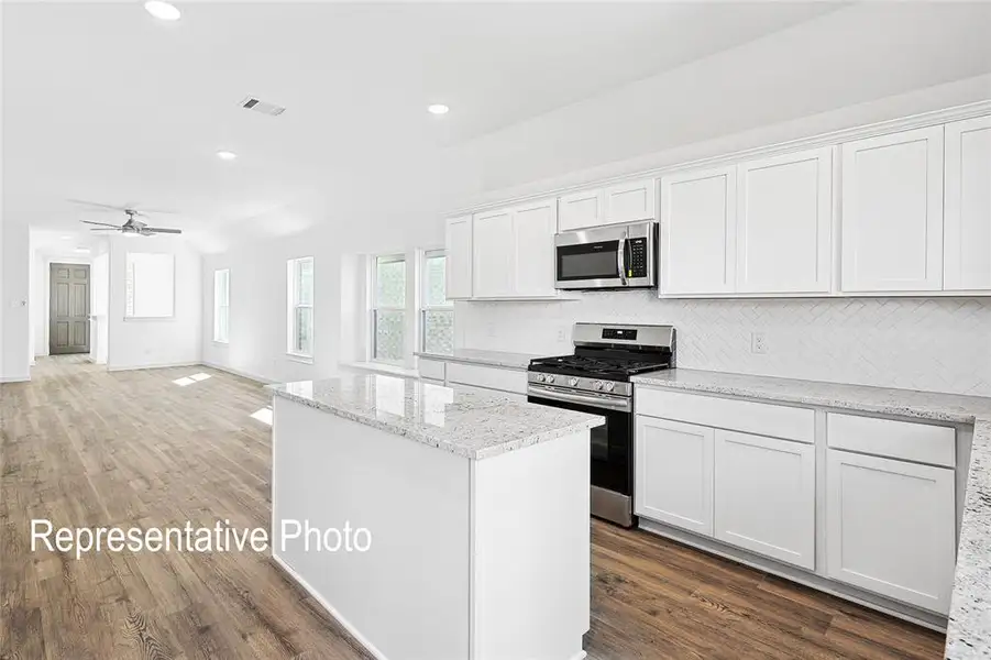 Open-concept kitchen featuring an island, white cabinetry, integrated stainless steel appliances, granite countertops, and a white herringbone tile backsplash