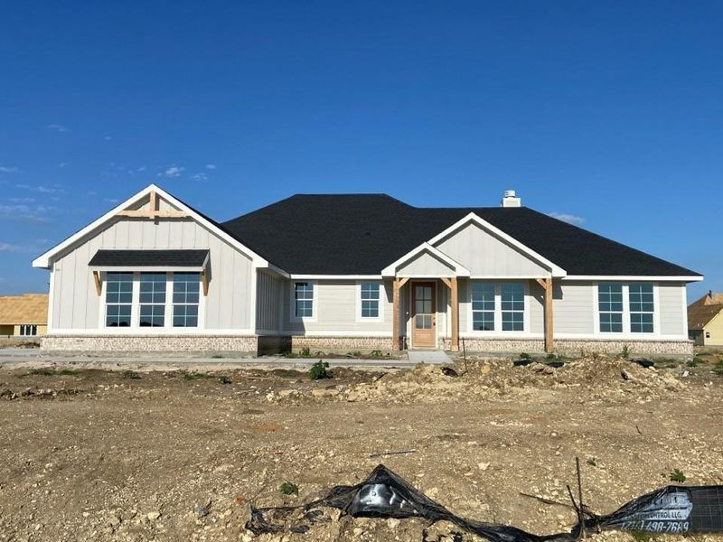 Contemporary farmhouse-style residence featuring a dark shingle roof, light-colored siding, and a stone foundation
