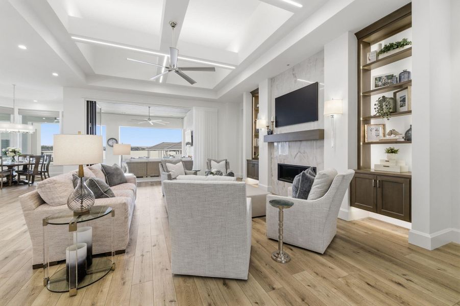 Living area with light wood finished floors, a high end fireplace, a tray ceiling, a ceiling fan, and built in shelves