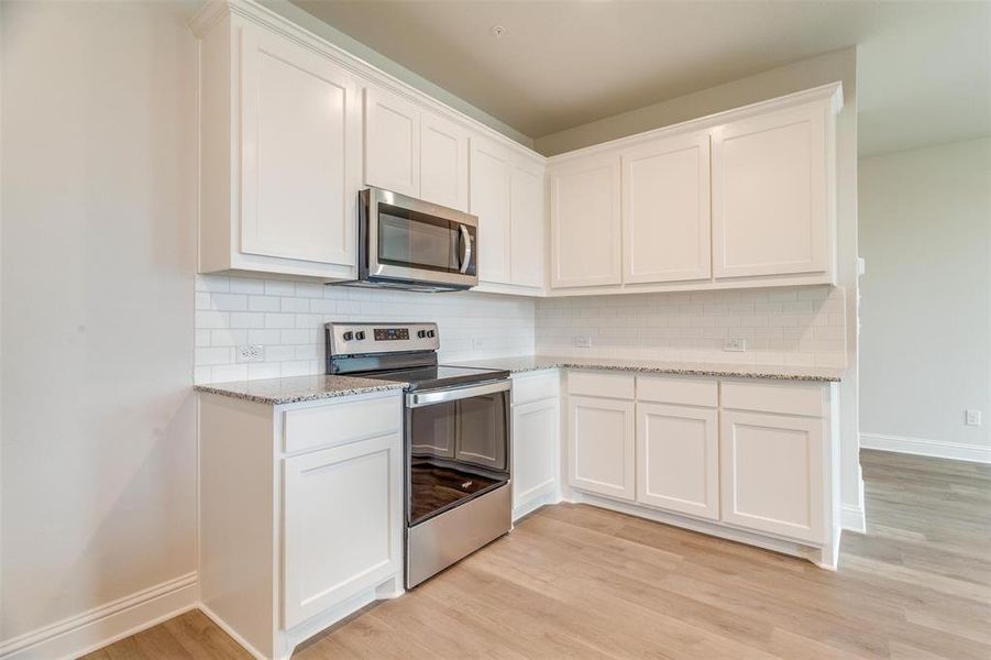 Kitchen with backsplash, light hardwood / wood-style floors, white cabinets, and appliances with stainless steel finishes