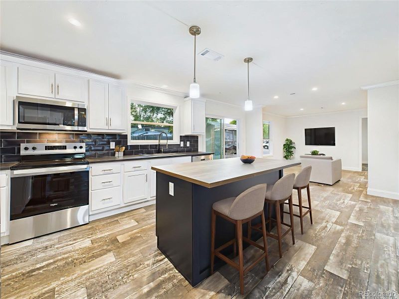 Virtually Staged Gourmet kitchen with white cabinetry, sleek black subway tile backsplash, and stainless steel appliances.