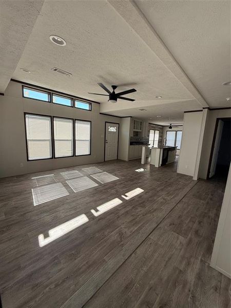 Unfurnished living room with dark wood-type flooring, a textured ceiling, and ceiling fan