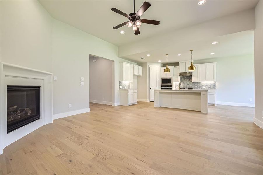 Unfurnished living room featuring recessed lighting, ceiling fan, a glass covered fireplace, light wood finished floors, and lofted ceiling Unfurnished living room featuring recessed lighting, ceiling fan, a glass covered fireplace, light wood finished floors, and lofted ceiling