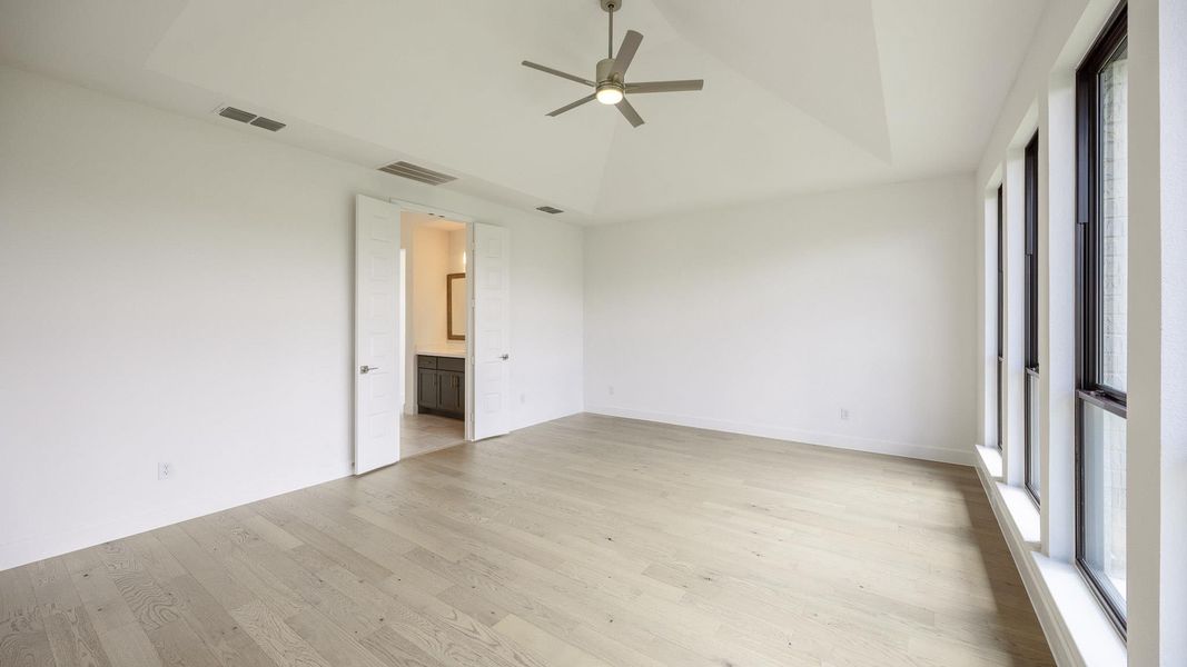 Unfurnished room with light wood finished floors, a raised ceiling, and a ceiling fan Unfurnished room with light wood finished floors, a raised ceiling, and a ceiling fan