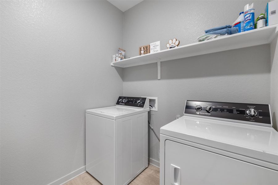 Laundry area featuring a textured wall, light wood-type flooring, and washer and clothes dryer Laundry area featuring a textured wall, light wood-type flooring, and washer and clothes dryer