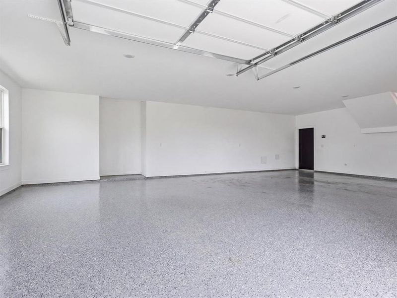 Expansive garage featuring a speckled epoxy floor finish, white painted walls, and a visible garage door track system