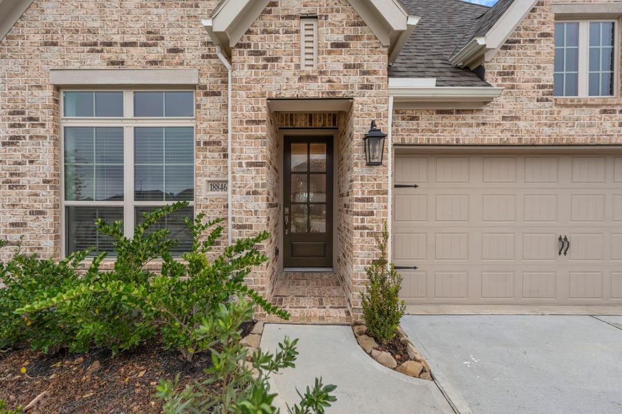 From the moment you arrive, this custom-built home impresses with curated upgrades and luxurious details at every turn. A charming covered front porch with classic brick flooring sets the tone, leading to a grand wood entry door with reeded privacy glass that makes a statement all its own. Truly exceptional craftsmanship—inside and out.