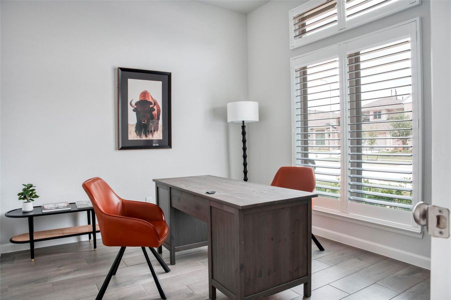 This bright and inviting home office features large windows with shutters, a sturdy wooden desk, and stylish orange chairs. A floor lamp and wall art add charm, while the view outside offers a glimpse of a well-kept neighborhood. This bright and inviting home office features large windows with shutters, a sturdy wooden desk, and stylish orange chairs. A floor lamp and wall art add charm, while the view outside offers a glimpse of a well-kept neighborhood.