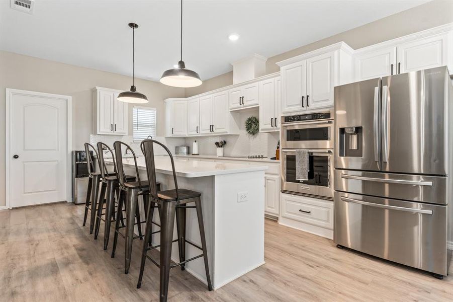 Bright kitchen with stainless steel appliances, a kitchen bar, a kitchen island, white cabinetry, and decorative light fixtures Bright kitchen with stainless steel appliances, a kitchen bar, a kitchen island, white cabinetry, and decorative light fixtures