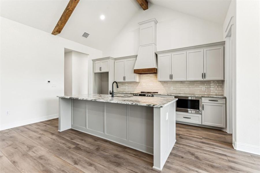 Kitchen with beamed ceiling, light stone countertops, an island with sink, and light hardwood / wood-style floors