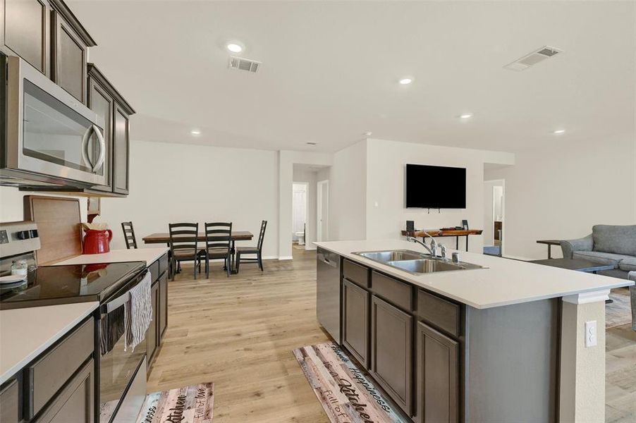 Kitchen with stainless steel appliances, an island with sink, light hardwood / wood-style floors, sink, and dark brown cabinets