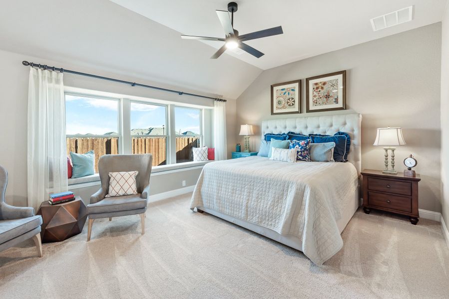 Bedroom with vaulted ceiling, ceiling fan, window seat, and sitting area with gray accent chair Bedroom with vaulted ceiling, ceiling fan, window seat, and sitting area with gray accent chair