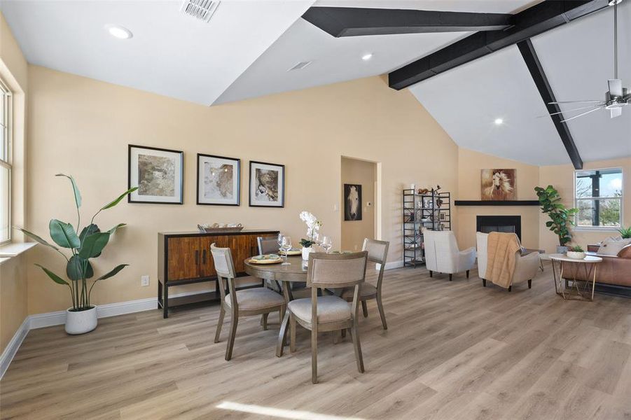 Open-concept living space featuring vaulted ceilings with exposed black beams, light wood-finish flooring, a built-in fireplace with a mantel, and recessed lighting Open-concept living space featuring vaulted ceilings with exposed black beams, light wood-finish flooring, a built-in fireplace with a mantel, and recessed lighting