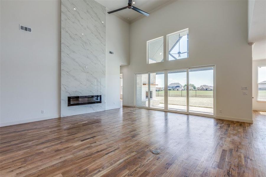 Unfurnished living room with ceiling fan, hardwood / wood-style flooring, a towering ceiling, and a high end fireplace