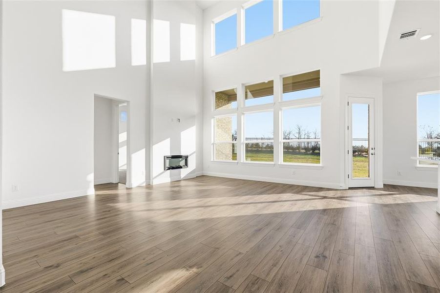 Unfurnished living room with light wood-type flooring and a high ceiling Unfurnished living room with light wood-type flooring and a high ceiling