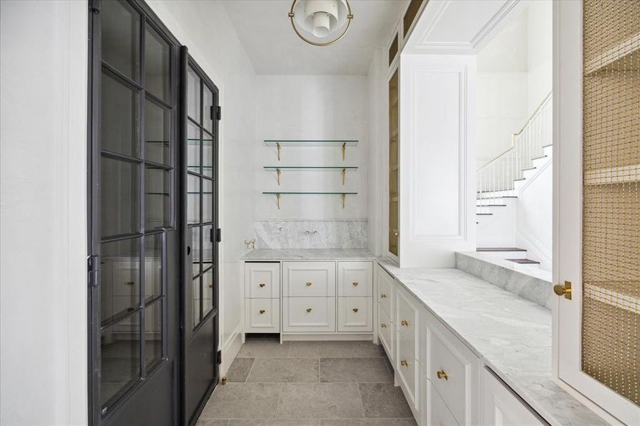 The handsome bar features glass floating shelves with gold accents, several built-in cabinets and shelves to store all of your glassware, and iron doors leading to the wine cellar.