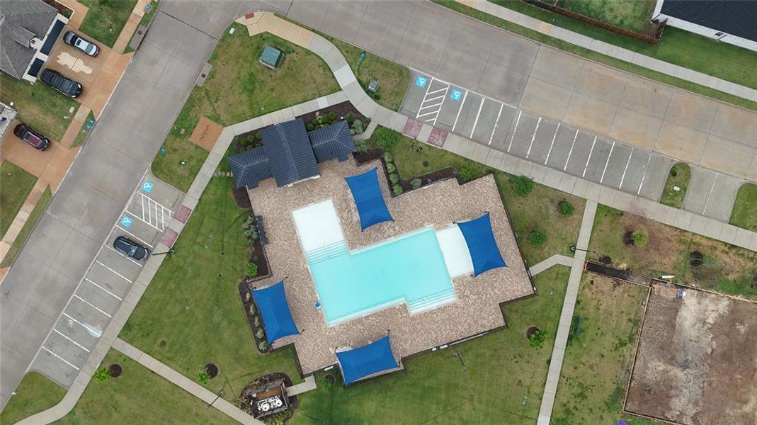 Aerial view showcasing the community pool area with a rectangular pool, surrounding paved deck, and blue shade structures
