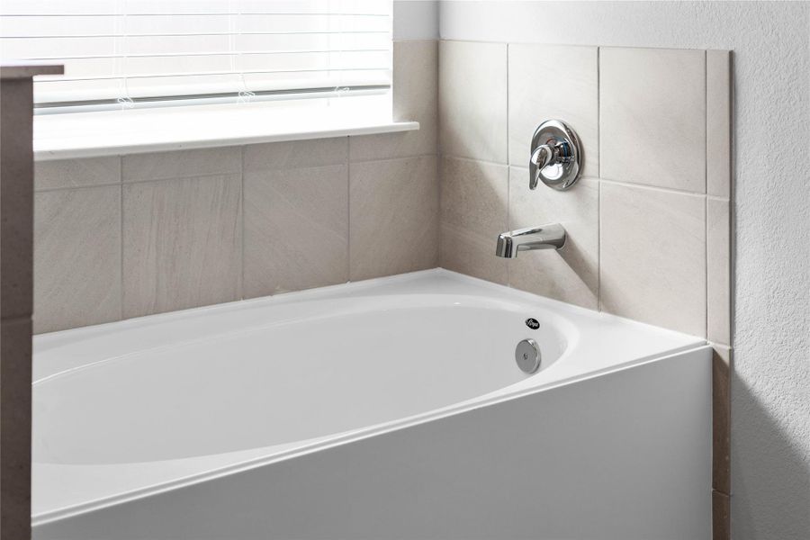 Indulge in the primary bath's deep, built-in soaking tub with elegant chrome fixtures and a sleek tile surround for a true spa-like retreat.