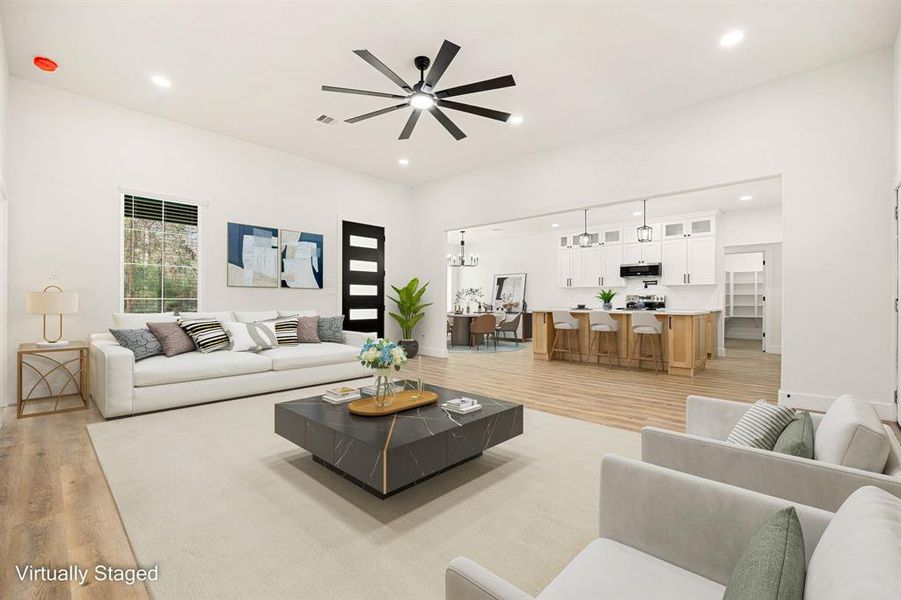 This photo showcases a spacious, open-concept living area with modern light fixtures, a large kitchen island with wooden cabinetry, and sleek flooring. Ample natural light pours in through multiple large windows, creating a bright and inviting atmosphere.