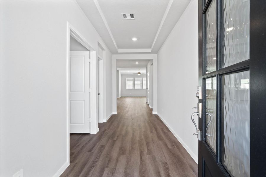 This entryway features a modern, open-concept design. The long, wide, and bright corridor utilizes a neutral color palette, recessed lighting, and Luxury Vinyl plank flooring to lead the eye toward the home's main living area.
