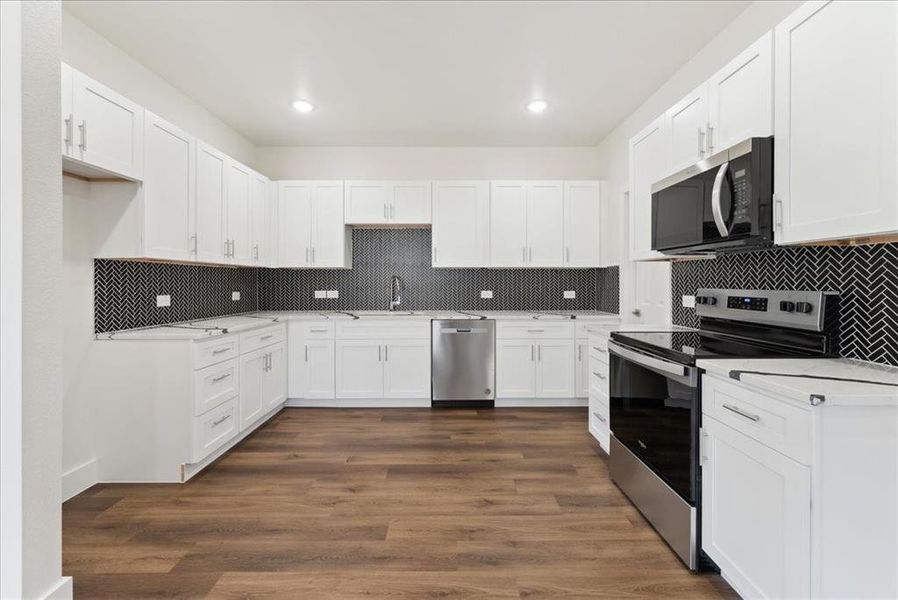 Kitchen featuring sink, backsplash,/ wood-style vinyl floors stainless steel appliances, and white cabinets, quartz counter tops