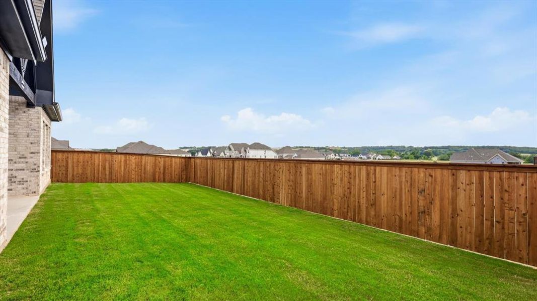 Expansive backyard featuring a manicured lawn, a stained wood privacy fence, and a concrete patio area