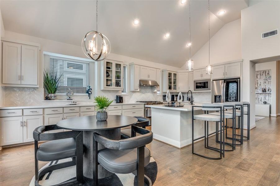 Kitchen featuring glass insert cabinets, decorative backsplash, hanging light fixtures, a breakfast bar, and an island with sink
