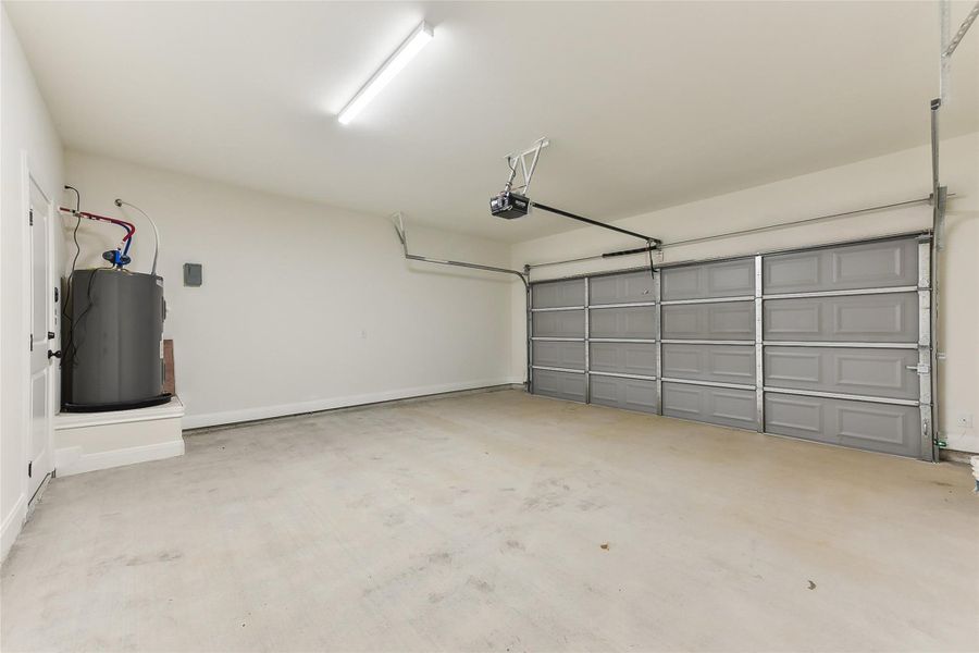 Garage featuring baseboards, a garage door opener, and electric water heater Garage featuring baseboards, a garage door opener, and electric water heater