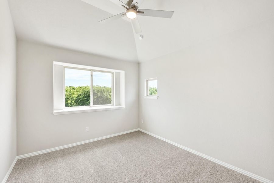 Empty bedroom with vaulted ceiling, ceiling fan, carpet flooring, and two windows with tree views Empty bedroom with vaulted ceiling, ceiling fan, carpet flooring, and two windows with tree views