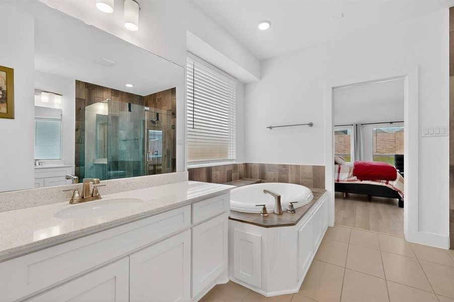 Bathroom featuring a built-in soaking tub, a separate glass-enclosed shower, a double vanity with stone-look countertops, and tile flooring Bathroom featuring a built-in soaking tub, a separate glass-enclosed shower, a double vanity with stone-look countertops, and tile flooring