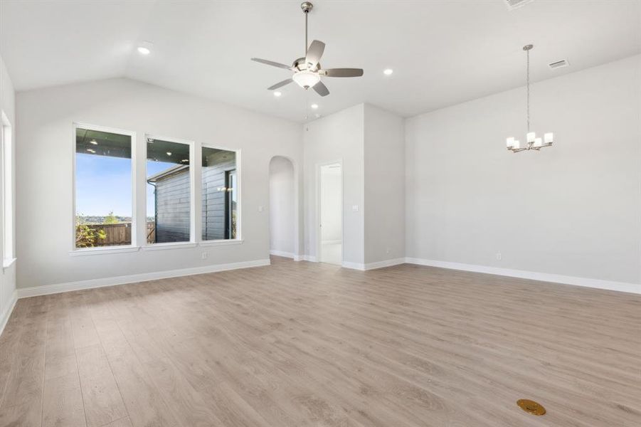 Unfurnished living room with light hardwood / wood-style flooring, ceiling fan with notable chandelier, and lofted ceiling