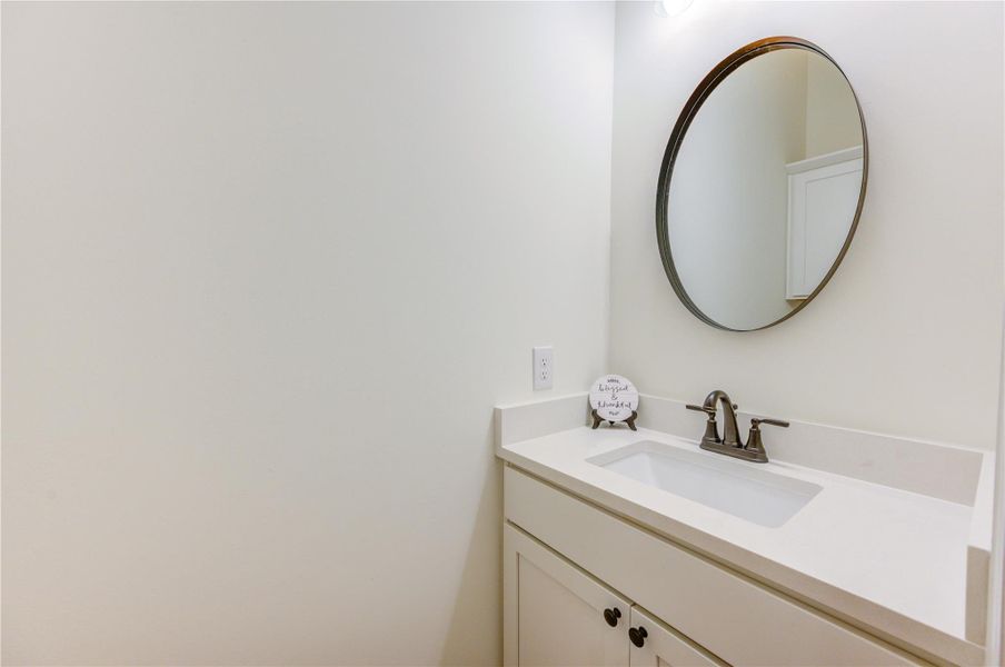 This half bath is a clean, modern bathroom with a white vanity, a round mirror, and sleek fixtures. The neutral color scheme creates a bright and inviting space. This half bath is a clean, modern bathroom with a white vanity, a round mirror, and sleek fixtures. The neutral color scheme creates a bright and inviting space.