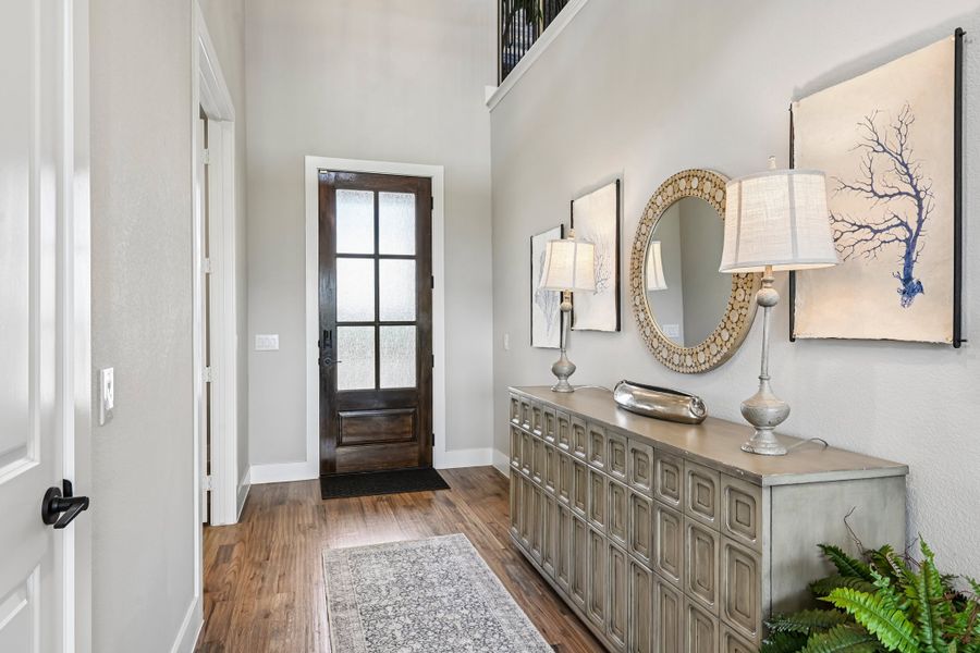 Entryway with dark wood glass-panel front door, console table, round mirror, and hardwood floors