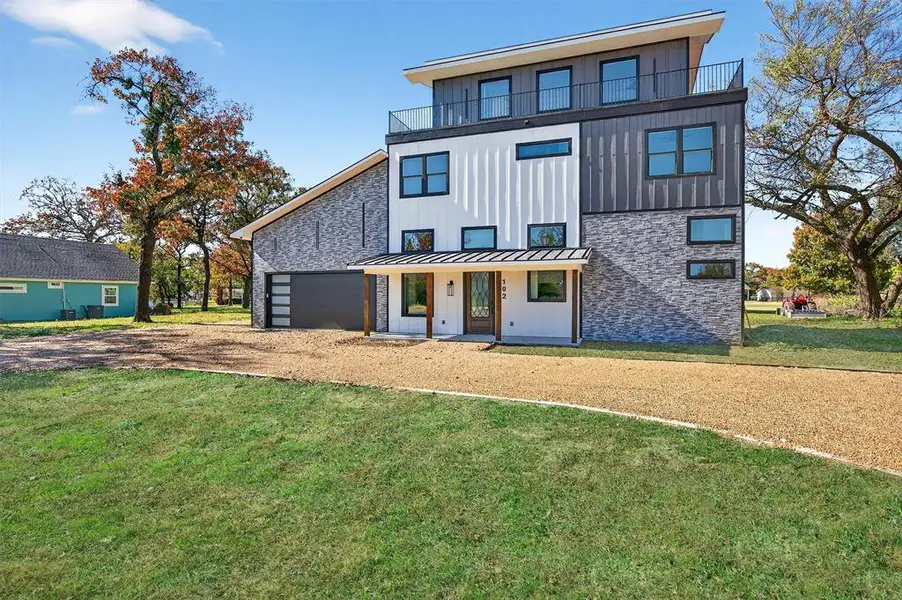 Back of house with a standing seam roof, a lawn, board and batten siding, a metal roof, and driveway
