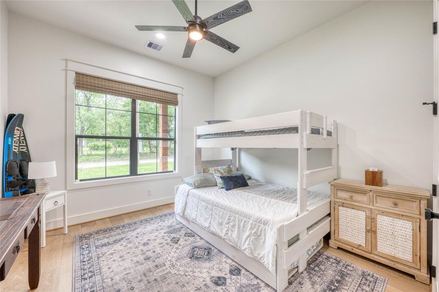 Bedroom featuring light wood-finish flooring, a large window with black framing, and a ceiling fan