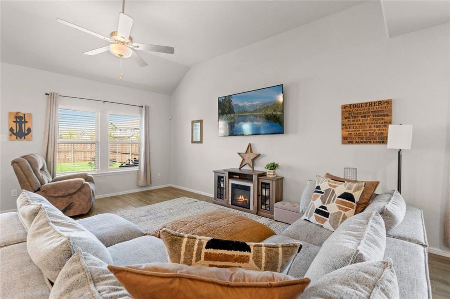 Downstairs living room featuring wood finished floors, a glass covered fireplace, lofted ceiling, and a ceiling fan