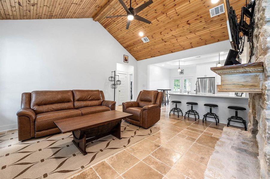 This open living space showcases vaulted wood-accented ceilings, stylish tile flooring, and a beautiful stone fireplace that serves as the focal point of the room. The seamless flow into the bar-style kitchen with seating makes the space ideal for gathering and entertaining.