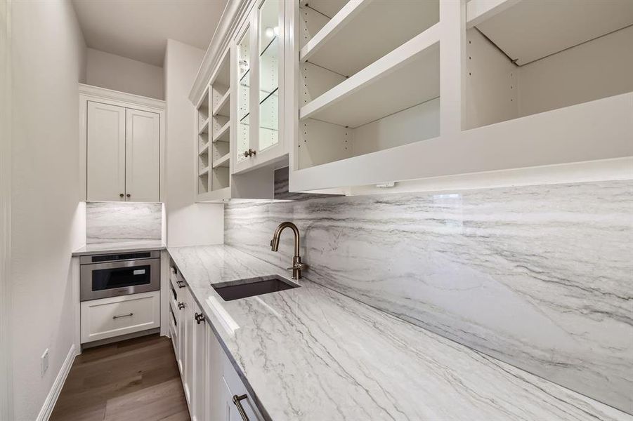 Working pantry featuring white cabinetry, microwave, sink, and light stone countertops